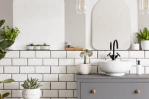 Real photo of a washbasin on a cupboard in a bathroom interior with tiles, mirror and plants