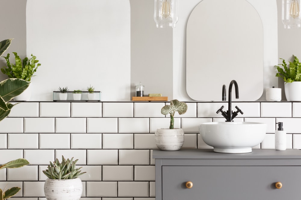 Real photo of a washbasin on a cupboard in a bathroom interior with tiles, mirror and plants