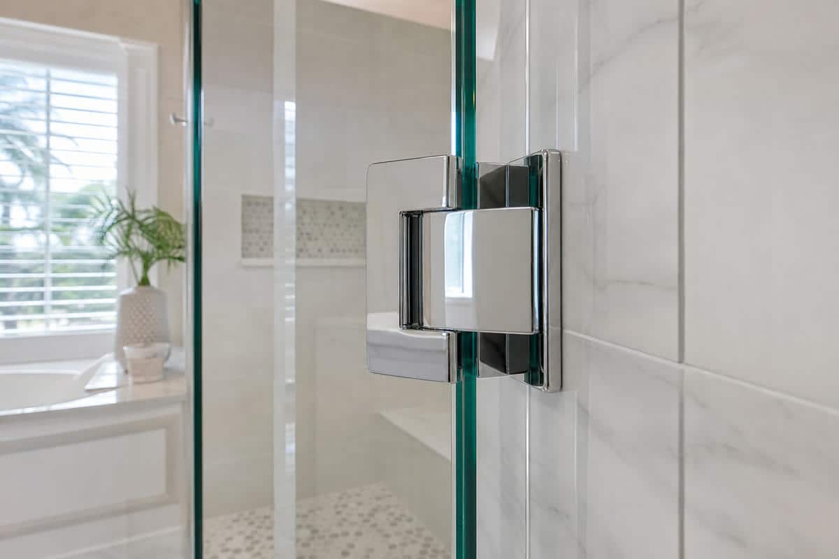 Close view of a frameless shower glass hinge mounted on tile