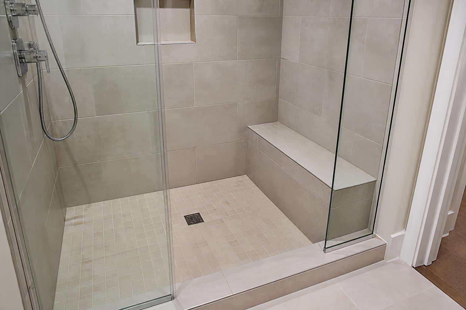 Tiled corner shower bench with grab bar and handheld sprayer nearby