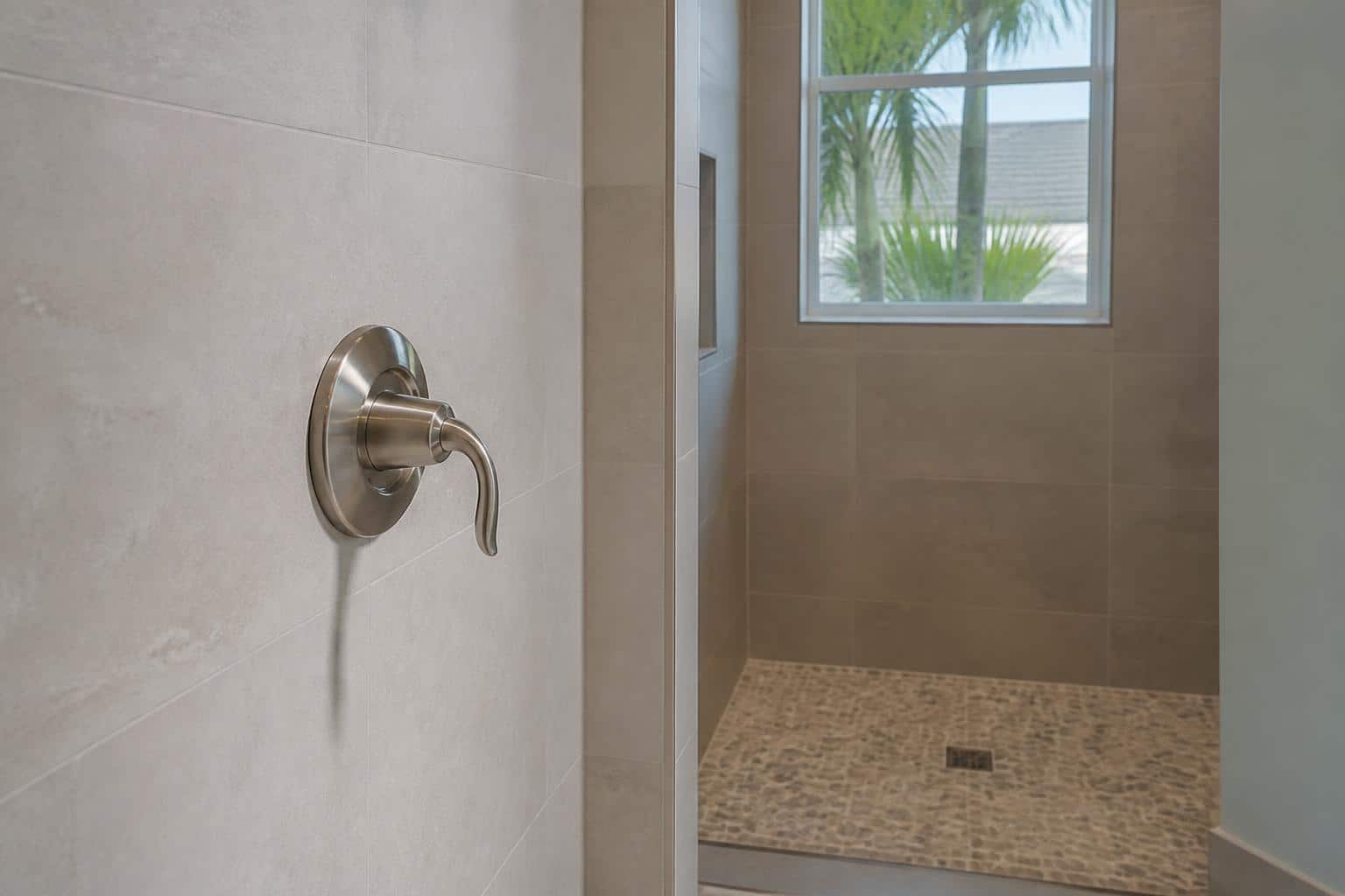 Close view of a shower valve and handle beside a tiled opening